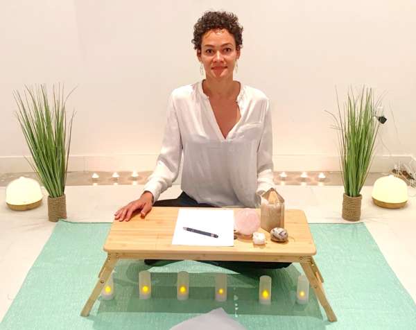 Contact - Aurélia Aubout assise en tailleur à une table avec des cristaux - Soins-Vibrations.com